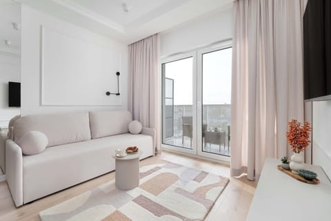 Bright living room with a large window, neutral-toned sofa, and light wooden flooring.