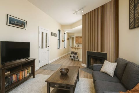 Living room with slat-wood fireplace surround, smart TV, and gray sectional, opening to the kitchen and breakfast bar.