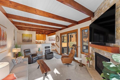 Relax in your spacious living room featuring exposed wood beams, a cozy stone fireplace, and modern seating perfect for unwinding after mountain adventures.
