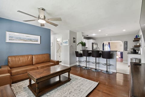 Relax in the open-concept living area featuring a leather sofa, flat-screen TV, and a modern kitchen with a breakfast bar for four. Perfect for enjoying meals, conversations, or cozy movie nights together.