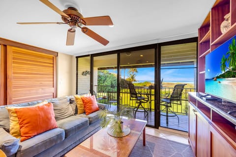 Relax in a bright living room featuring a cushioned sofa with colorful accent pillows, a ceiling fan overhead, and wide glass doors that open to scenic outdoor views.