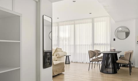 A bright dining and living area featuring a round dining table, sleek chairs, and large windows.