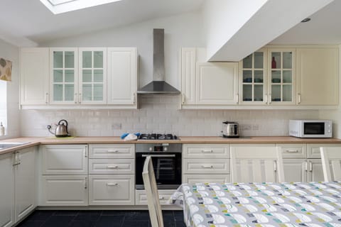 A bright, spacious kitchen with ample counter space, cabinet lighting, dishwasher, etc, and all essentials. Features a six-seater dining table, two-seater sofa, and double doors opening to the large garden—perfect for cooking, dining, and relaxing.