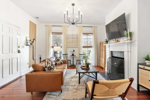 Sun-filled living room with cognac leather sofa, decorative fireplace, and original hardwood floors in this renovated downtown Savannah Victorian flat.