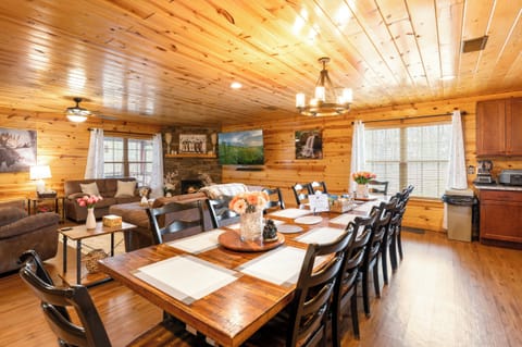 Warm cabin great room—12-seat table, stone fireplace, bright and cozy.