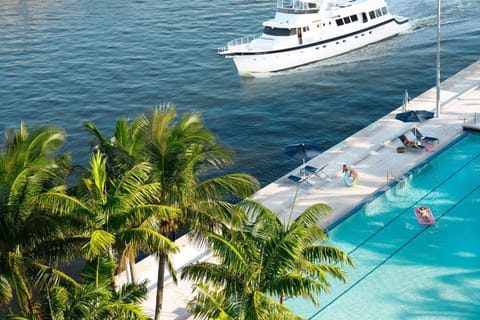 Waterfront pool deck framed by palms and passing yachts