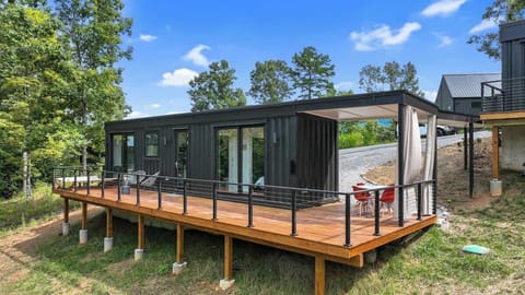 This sleek container home features a spacious deck, covered outdoor dining area, and peaceful wooded views.