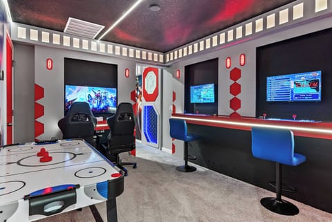 Welcome to our vibrant game room, filled with bold red and blue accents. Enjoy sleek gaming chairs and dual screens for non-stop fun. The air hockey table invites friendly competition, creating a lively hub for guests of all ages.