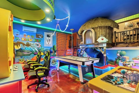 Welcome to our vibrant game room, where energy fills the air and colorful decor creates a cheerful atmosphere. With glossy red floors, bright blue walls, comfortable gaming chairs, and a sleek air hockey table, fun awaits for all!