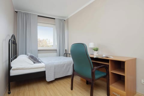 A bright bedroom with a double bed, desk, and chair next to a large window. The space feels clean and ideal for studying or relaxing.