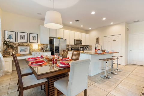 This inviting kitchen boasts sleek white cabinetry and a spacious island ideal for culinary creativity. A warm wood dining table with vibrant red accents enhances every meal, seamlessly connecting cooking and dining experiences.