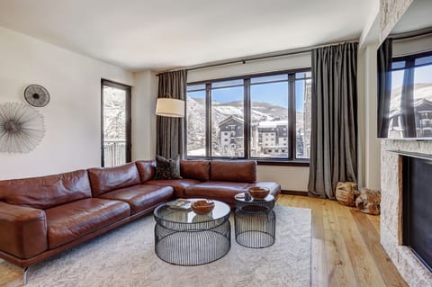Elegant living area with plush leather sectional, gas fireplace, and oversized windows overlooking Lionshead Village.