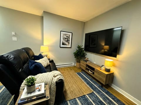 Cozy living area with leather seating, wall-mounted TV, floor lamp, and area rug.