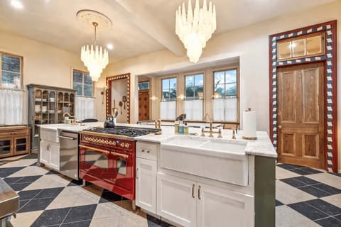 Chef’s kitchen with a large center island, farmhouse sinks, a high-end red range, and statement chandeliers.