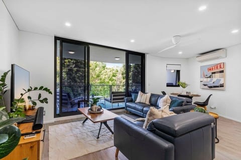 Bright lounge with 65-inch Smart TV, seating and open kitchen flow.