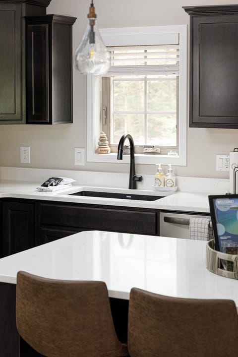 Sunlit kitchen sink area w/ window views & clean, modern counters.