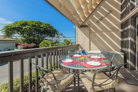 A relaxed open-air space for outdoor dining with partial overhead coverage, featuring a peek of the Pacific through lush tropical foliage and sunshine filtering onto your table.
