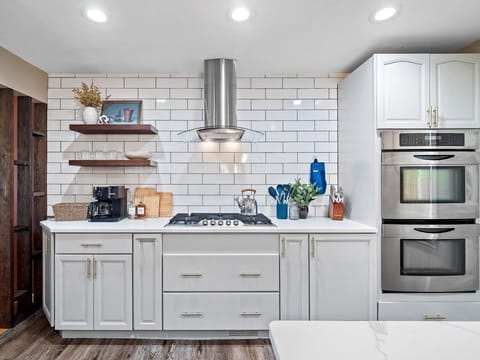 Cook in style! 🍳 This bright kitchen features a gas stove, double ovens, and sleek subway tile. Enjoy the coffee station, wood shelves, and gold accents for a true luxury feel ☕️✨