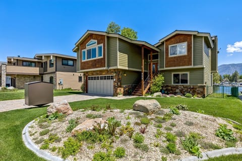 Exterior view of the house with stone accents, green siding, and a landscaped front yard under a clear blue sky.