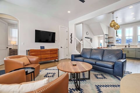 This wide view shows the open living room with plush seating, a Smart TV, and easy flow into the dining nook and kitchen. Soft colors and layered textures create a comfortable, inviting gathering space.