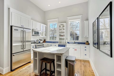 A spacious kitchen with tall windows, marble counters, and an island with seating creates an easy, functional space for cooking and gathering.