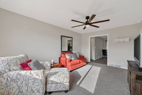 Bright, cozy living room with plush seating, a stylish coral loveseat, and a comfy patterned armchair. Enjoy natural sunlight, a modern ceiling fan, and a flat-screen TV…perfect for relaxing after a long day or movie nights in.