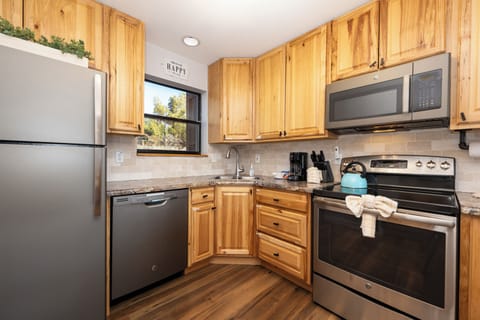 Cook with ease in your fully equipped kitchen, featuring warm wood cabinets, granite counters, and stainless steel appliances including dishwasher and microwave.