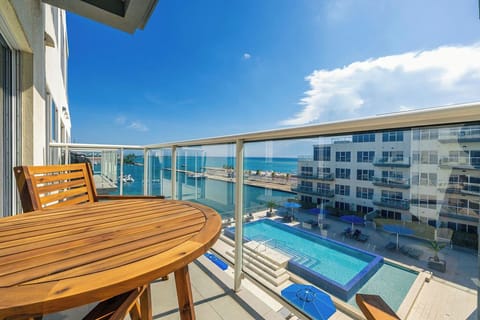 A modern balcony with ocean views and pool courtyard overlooks an inviting waterfront property under clear skies.