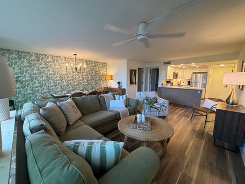 Relax on your plush sectional sofa in this open-concept living space featuring tropical-inspired decor and a sleek kitchen with modern appliances.
