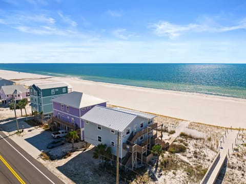 Colorful beachfront homes line pristine white sand with crystal-clear waters stretching to the horizon under brilliant blue skies.
