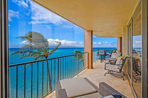 Balcony with cushioned chairs and table, sea breeze brushing your skin as waves shimmer endlessly below.