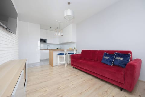 Bright living area featuring a red sofa, wall-mounted TV and an open-plan kitchen filled with natural light.