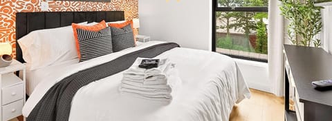 Stylish bedroom with bold patterned wallpaper, cozy queen bed, and bright natural light—your perfect urban retreat.