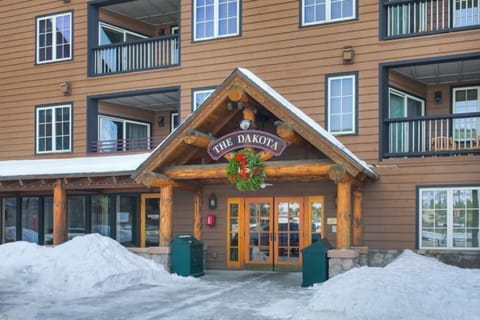 In a winter wonderland, the Dakota Lodge entrance adorned with a festive wreath stands ready to greet visitors eager for skiing adventures.