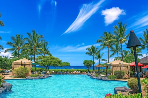Lagoon-style pool with tiki torches and cabanas set against brilliant blue skies and Maui’s stunning coastline HKH-211