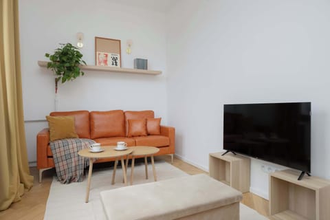 Cozy living area featuring a caramel sofa, soft rug, modern TV stand and warm decorative accents.