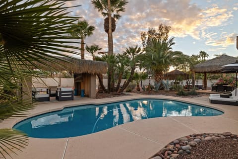Tropical backyard oasis with pool, palm trees, and cozy tiki-style cabanas.