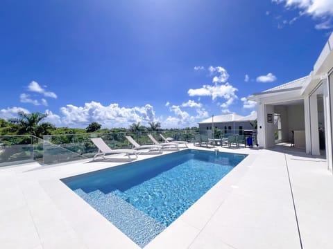 Stunning modern pool with sleek design, surrounded by comfortable loungers and a bright terrace. Enjoy a beautiful open view of lush greenery and blue skies — the ideal spot for relaxing moments in the sun.