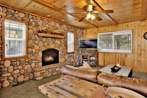 Cozy mountain living room with a stone fireplace, comfy seating, and smart TV—perfect for relaxing evenings, movie nights, and warm cabin vibes after outdoor adventures.