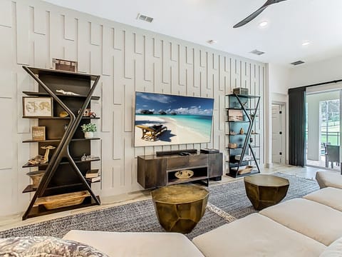 Stylish and spacious living room featuring modern décor, a large flatscreen TV, and direct access to the pool area for seamless indoor–outdoor living.