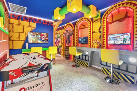 Enter a lively game room filled with playful colors and fun decor, featuring bright yellow bar stools, a classic pinball machine, and vibrant murals, perfect for sparking friendly competition and endless entertainment.