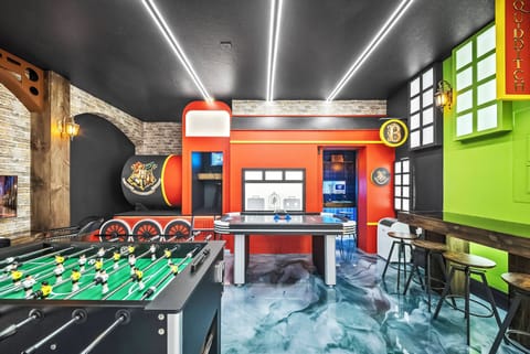 Welcome to our lively entertainment room with a bold orange bar for gatherings, sleek black accents, and cheerful green walls. Enjoy friendly competition at the foosball table and immerse yourself in the vibrant atmosphere!