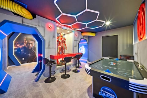 Discover a lively entertainment room with vibrant neon accents and playful decor, including a life-sized Iron Man statue. Enjoy a game night with friends at the fun game table and relax on the sleek bar stools.