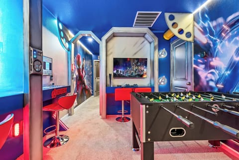 Step into a vibrant game room where playful blue walls set the stage for fun. Enjoy friendly competitions around the foosball table, surrounded by striking artwork and sleek red bar stools that invite laughter and camaraderie.
