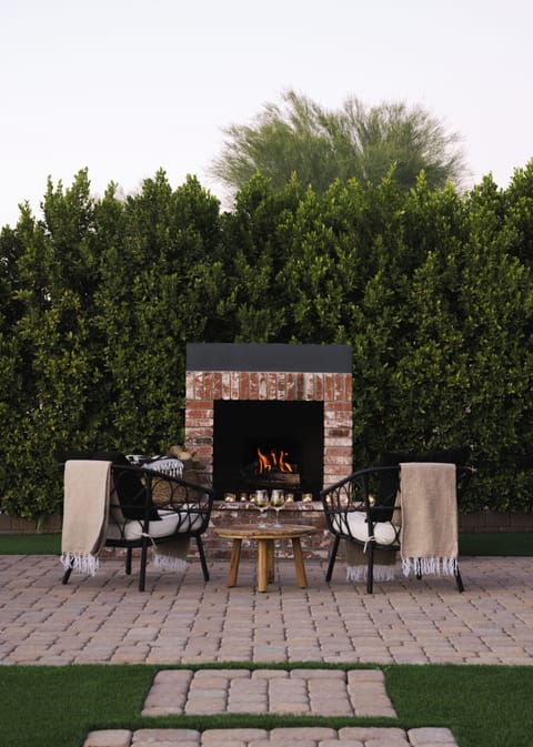 Wood-burning fireplace with a mature wall of greenery as the backdrop.