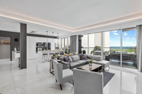 Sleek modern living space with stunning ocean views through floor-to-ceiling glass doors. Relax in the open-plan lounge with stylish gray seating, gleaming white tiles, and seamless indoor-outdoor flow.