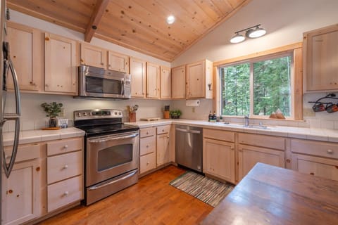 Picture yourself preparing meals in this inviting kitchen with its beautiful wood ceiling and cabinets. Natural light streams through the window above the sink, offering peaceful forest views while you cook.