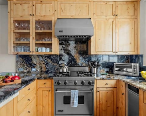Fully-equipped kitchen featuring natural wood cabinetry and striking dark granite countertops and backsplash. Includes a stainless steel gas range/oven (Viking), a matching range hood, and a toaster oven. 