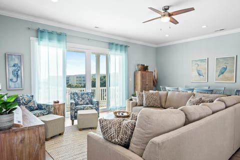 Relax in this coastal-inspired living room with soft blue accents and plush seating overlooking peaceful balcony views.