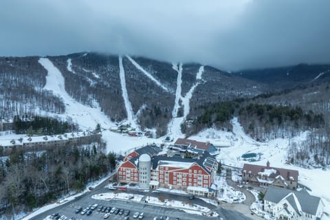 Aerial view of a ski resort nestled in snow-covered mountains with multiple ski slopes and trails descending through forested terrain.